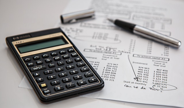 Black calculator neat silver ballpoint pen on white printed paper with numbers on it
